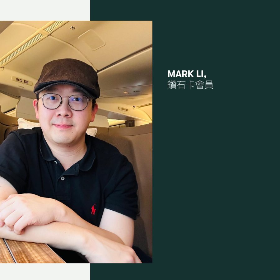 A man with glasses wearing a black polo shirt and a cap sits in the Business class cabin of a Cathay Pacific aircraft.